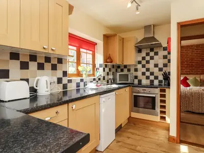 a kitchen with wooden cabinets and black counter tops at Poppy Cottage in Little Glenham