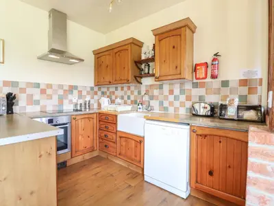 a kitchen with wooden cabinets and a white dishwasher at Barn Owl Cottage in Little Glenham