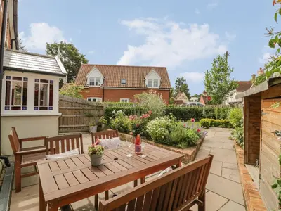 a patio with a wooden table and benches at Mulberry Cottage in Hadleigh
