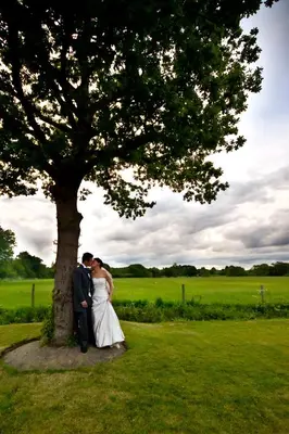 a bride and groom standing next to a tree at The Bull at Great Totham Limited in Great Totham