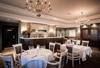 a restaurant with white tables and chairs and a chandelier at The Bull at Great Totham Limited in Great Totham