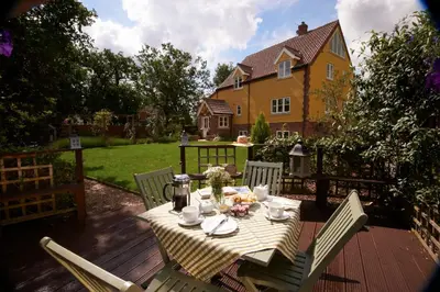 a table and chairs on a deck with a house at Sunset House Bed and Breakfast in East Harling