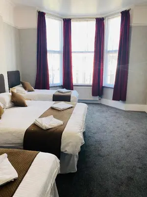 a hotel room with four beds with red curtains at The Grosvenor in Clacton-on-Sea