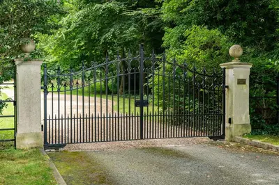 a black iron gate with a driveway and trees at Hertford Barn conversion in Hertford