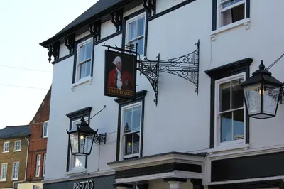 a white building with a sign on the side of it at The George Hotel Stansted Airport in Bishops Stortford