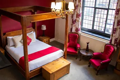 a bedroom with a canopy bed and two red chairs at The Scole Hotel in Scole
