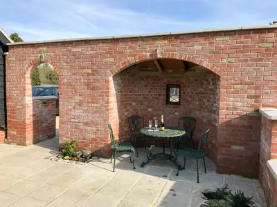 a patio with a table and chairs in a brick wall at Chick Hatch Barn in Kelsale