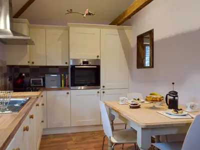 a kitchen with white cabinets and a table with chairs at Chick Hatch Barn in Kelsale