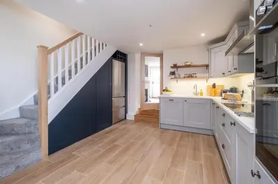 a kitchen with white cabinets and a staircase at Avocet Cottage in Aldeburgh