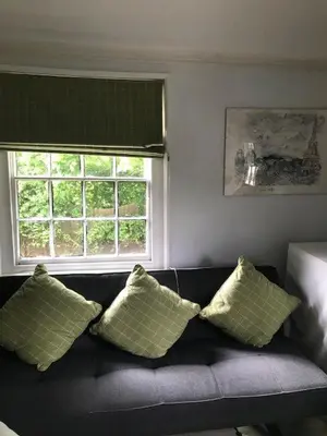 a couch with four pillows in a living room with two windows at The White House in Bishops Stortford