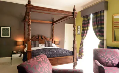 a bedroom with a canopy bed and a chair at Satis House Hotel in Yoxford