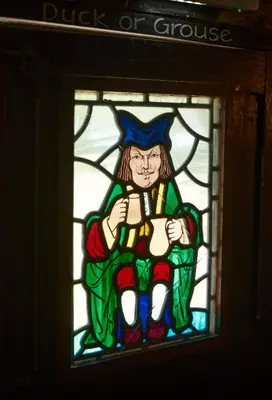 a stained glass window of a man sitting on a stool at Old Ferry Boat by Greene King Inns in St Ives