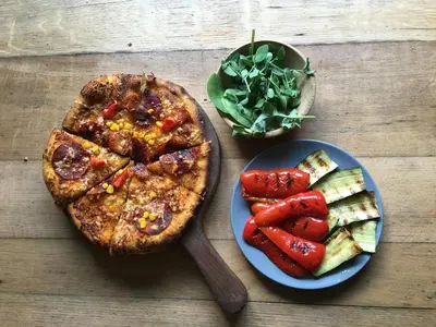 a table with a pizza and a plate of vegetables at Watt Cottage in Ipswich
