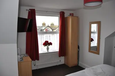 a bedroom with a window with red curtains and a vase of flowers at Victoria Villa Guesthouse in Clacton-on-Sea