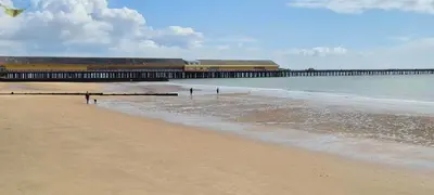 a beach with a pier and the ocean with a kite at Endymion Lodge in Colchester