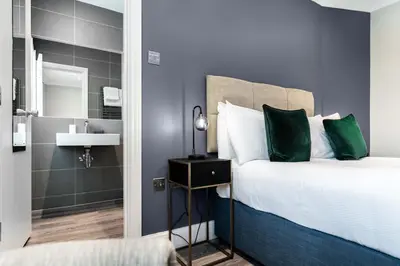 a bedroom with a bed with green pillows and a sink at The Regent Aparthotel in Cambridge
