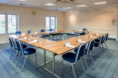 a conference room with wooden tables and chairs at Holiday Inn Colchester by IHG in Colchester