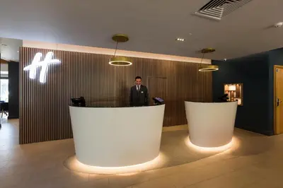 a man standing at a counter in a lobby at Holiday Inn Cambridge by IHG in Cambridge