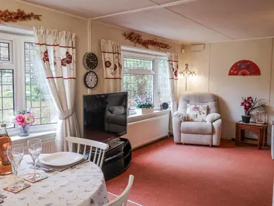 a living room with a table and a television and a chair at The Lodge in Attleborough