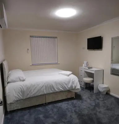 a bedroom with a bed and a desk and a television at Zaheer's Hotel in Baldock