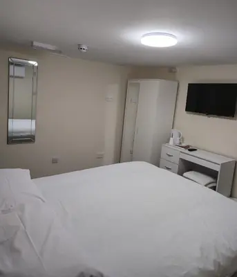 a bedroom with a large white bed and a desk at Zaheer's Hotel in Baldock