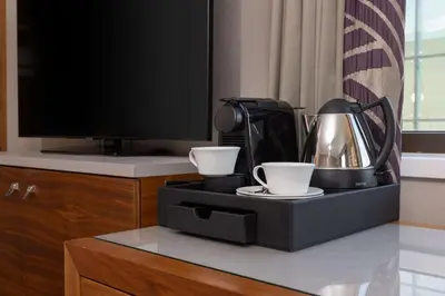 a coffee maker and two cups on a table with a tv at Hilton Cambridge City Centre in Cambridge