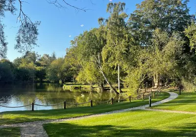 a park with a path next to a lake at Great Hallingbury Manor & Lodges London Stansted in Bishops Stortford