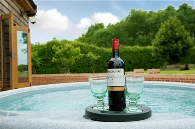 a bottle of wine and two glasses next to a swimming pool at Corner Farm in Halesworth