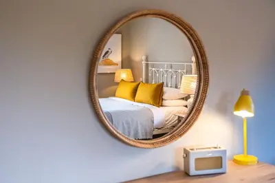 a mirror on a wall above a bed with yellow pillows at The Crown Inn in Stoke by Nayland