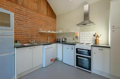 a kitchen with white cabinets and a brick wall at The Dairy Cottage in Aldeburgh