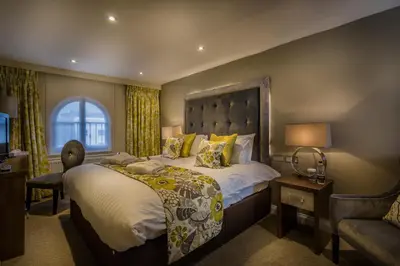 a bedroom with a large bed and a chair at The Golden Lion Hotel, St Ives, Cambridgeshire - The Coaching Inn Group in St Ives