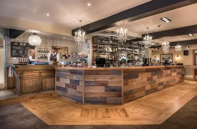 a bar in a restaurant with people standing at a counter at The Golden Lion Hotel, St Ives, Cambridgeshire - The Coaching Inn Group in St Ives