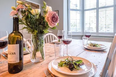 a table with a vase of flowers and a bottle of wine at Hillcrest, Aldeburgh in Aldeburgh