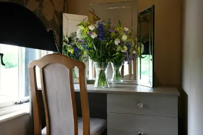 a vase of flowers on a dresser with a mirror at The White Hart in Great Yeldham