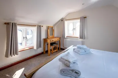 a bedroom with a bed and a desk and two windows at 3 Beach Cottages - Aldeburgh Coastal Cottages in Thorpeness