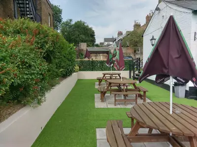 a row of tables and benches with an umbrella at The Rifle Volunteer in Ware