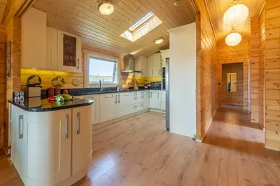a large kitchen with white cabinets and a wooden ceiling at The Lodge in Stowmarket