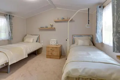 a bedroom with two beds and a nightstand and windows at Mersea Island by Away Resorts in Colchester