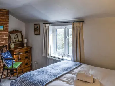 a bedroom with a bed and a window and a chair at Lavenham Red Brick Cottage in Lavenham