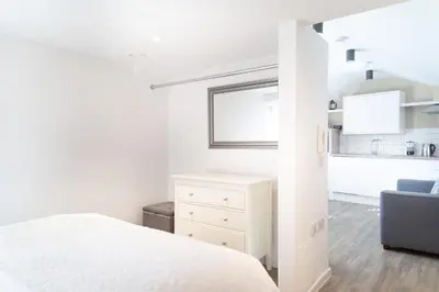 a white bedroom with a white bed and a kitchen at Citystay Living - Devonshire Road in Cambridge