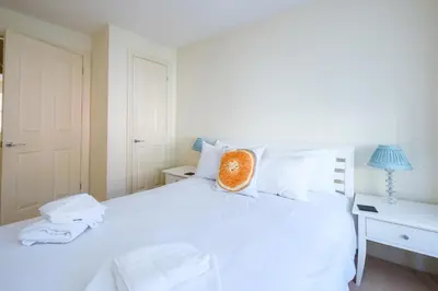 a bedroom with a white bed with an orange pillow on it at Maisie's in Aldeburgh