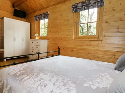 a bedroom with a bed and wooden walls and windows at Acorn Lodge in Saxmundham