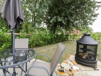 a table and chairs with a grill and an umbrella at Acorn Lodge in Saxmundham