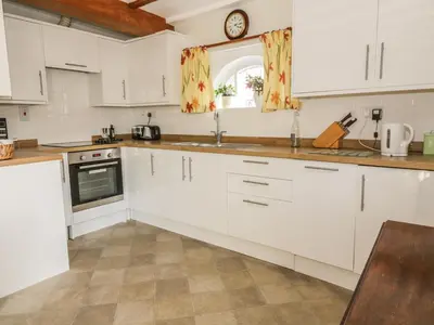 a kitchen with white cabinets and a clock on the wall at Stable Cottage in Sudbury