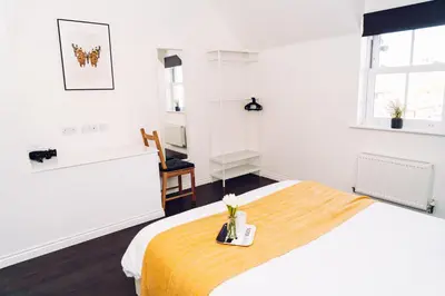 a white bedroom with a bed with a yellow blanket at Detached Coach House in Colchester