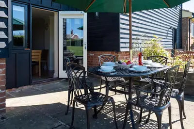 a table with chairs and an umbrella on a patio at Meadow View, Near Aldeburgh in Aldringham