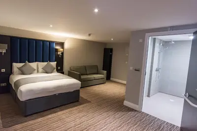 a bedroom with a bed and a chair and a shower at St Nicholas Hotel Colchester in Colchester