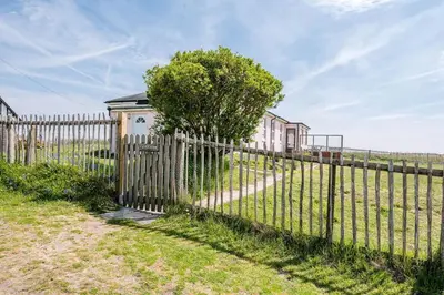 a fence with a tree next to a house at Fairhaven, Thorpeness in Thorpeness