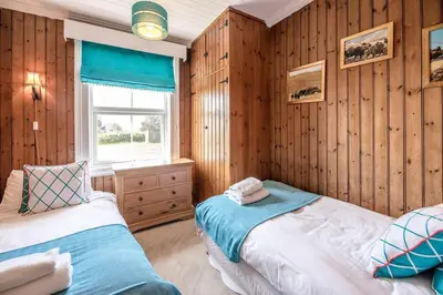 two beds in a room with wooden walls and a window at Fairhaven, Thorpeness in Thorpeness