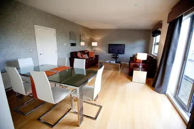 a dining room with a glass table and white chairs at Chelmsford Serviced Apartments in Chelmsford